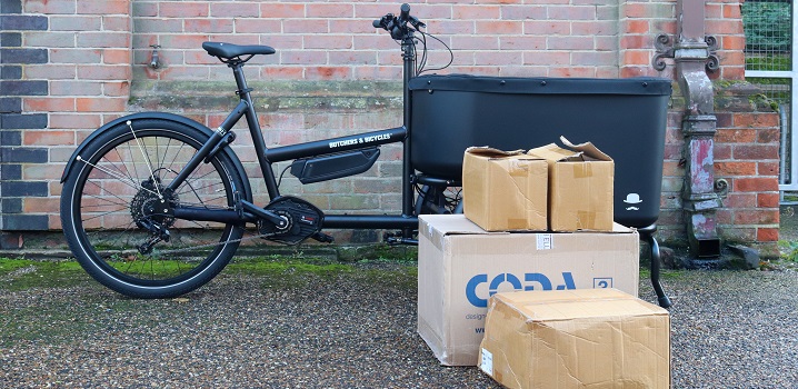 Black electric delivery bike beside six cardboard boxes